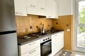 A kitchen with white cabinets, a gas stove, an oven, and a window with a view of greenery. - N084 - Numana, villa with garden and pool (Numana)