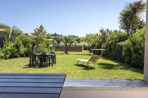 A patio with a table and chairs, surrounded by greenery and a wooden fence. - N084 - Numana, villa with garden and pool (Numana)