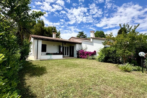 A house with a white exterior, a tiled roof, and a small garden with various plants.
