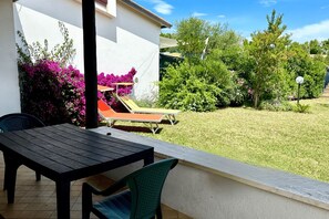 An outdoor patio with a table and chairs, a sun lounger, and a garden with various plants and trees.