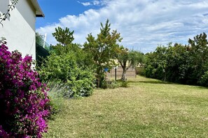 A well-maintained garden with a variety of plants and trees, a clear sky, and a building in the background.