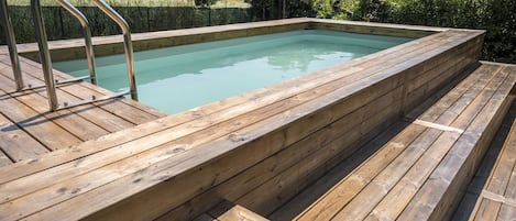 Piscina retangular de madeira com escada de metal sobre um deck de madeira.