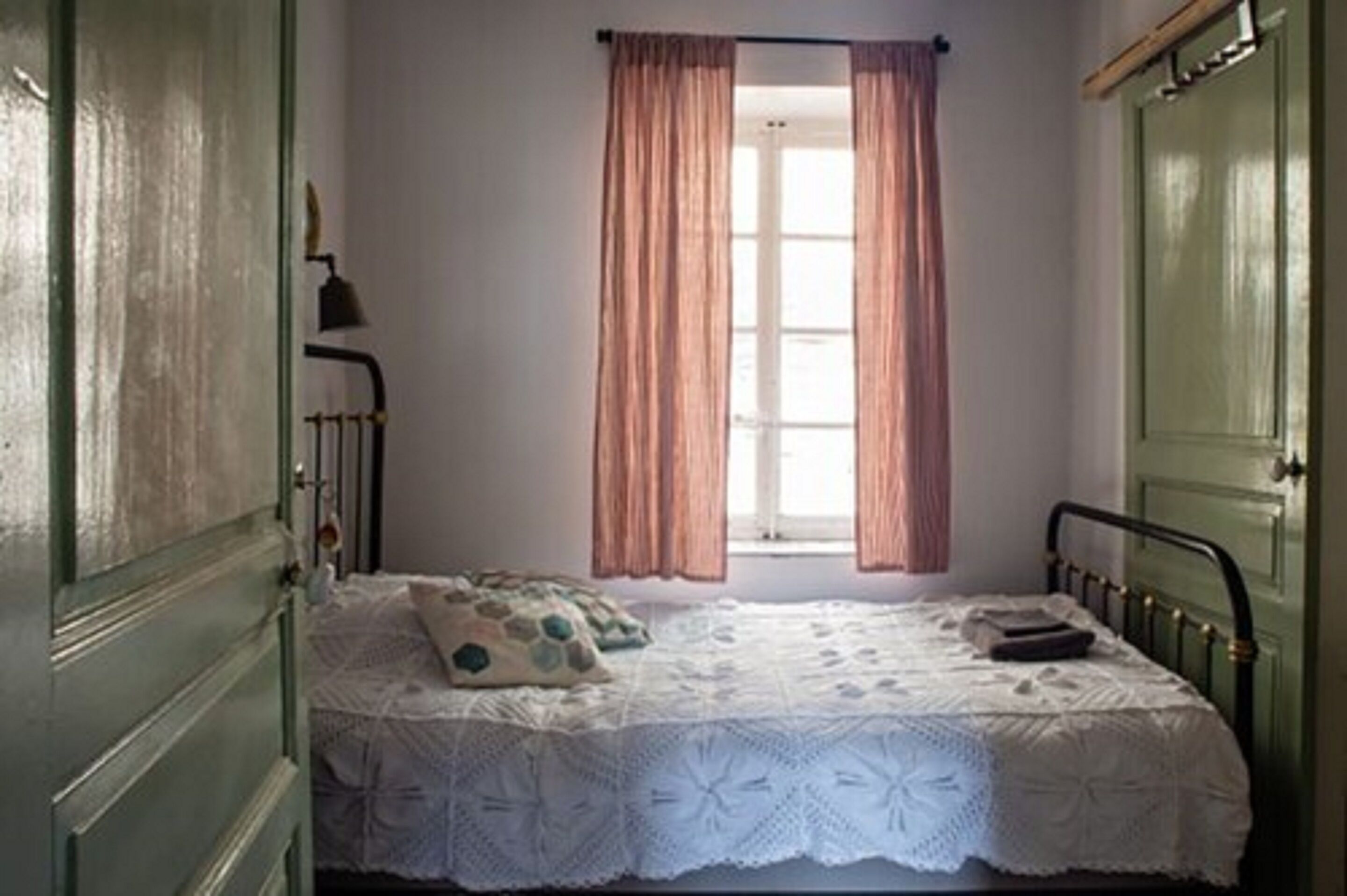Una habitación con una cama individual, una ventana con cortinas y una puerta.