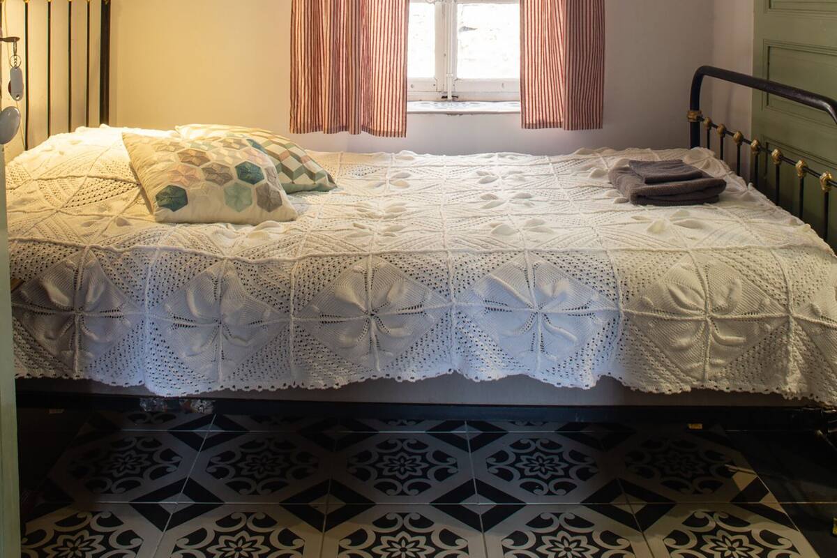 Un dormitorio con cama, un candelabro, una ventana con cortinas y una puerta verde.