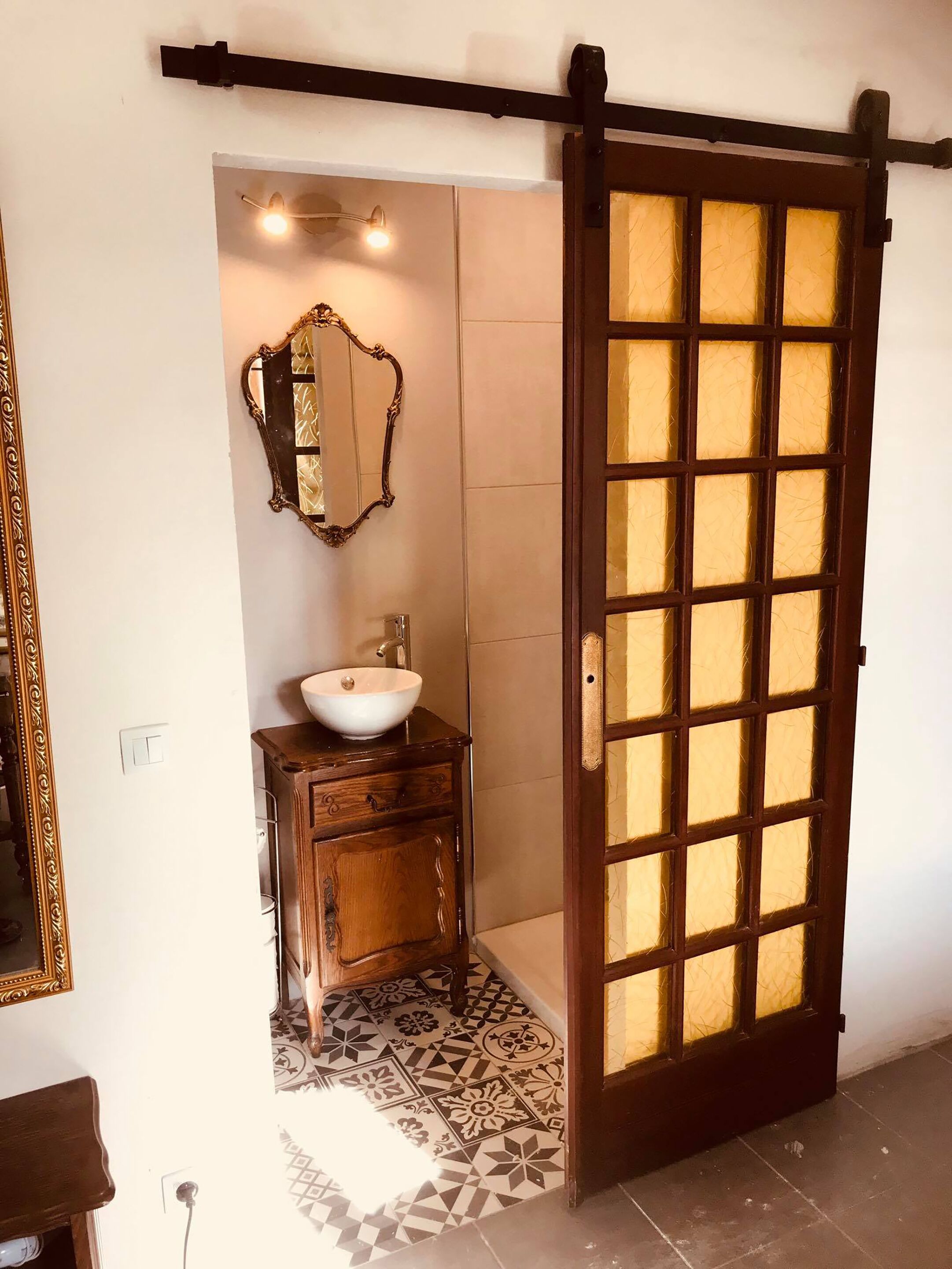 Een badkamer met een houten wastafel, een witte wasbak, een spiegel en een schuifdeur van glas.