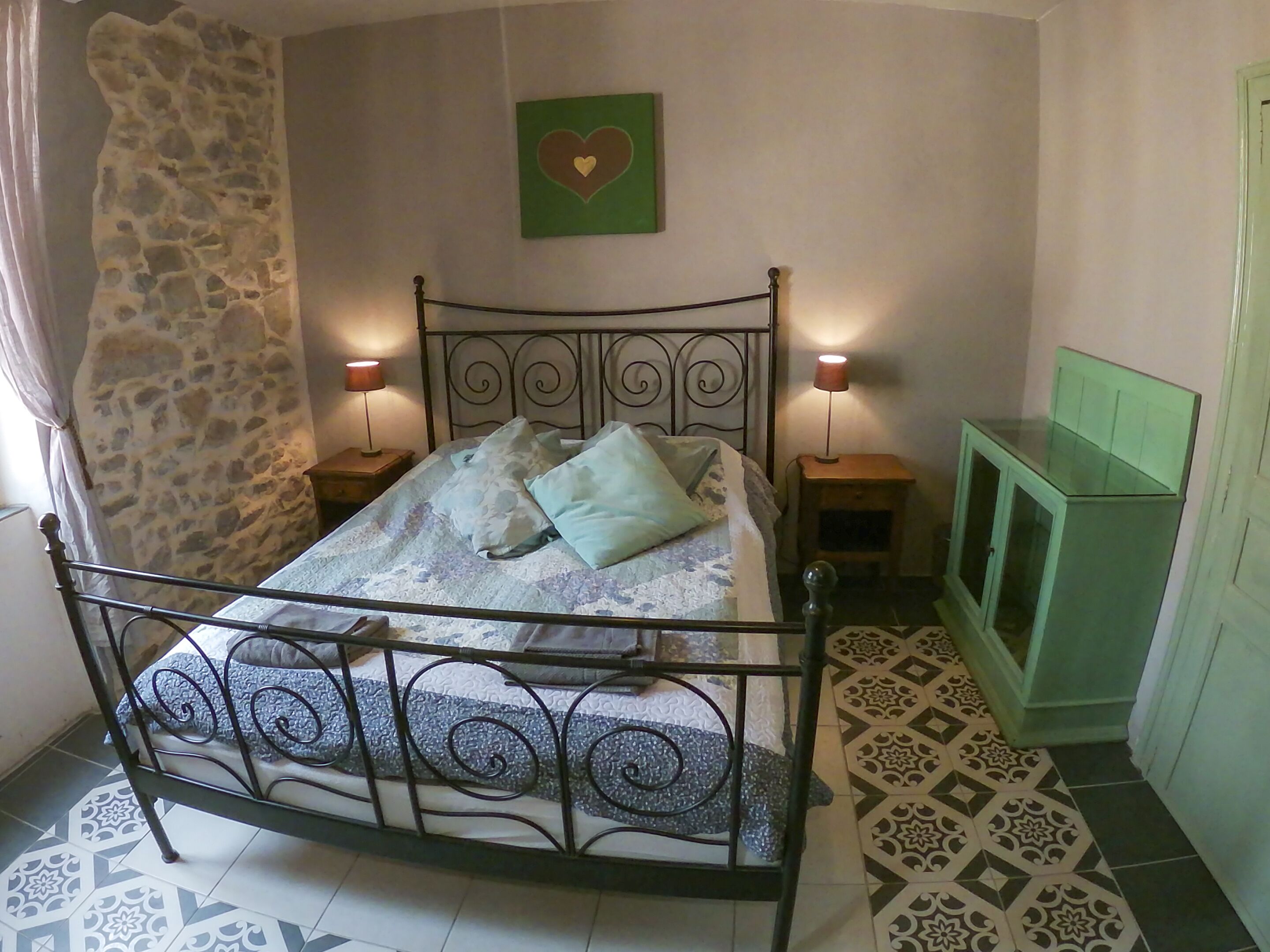 Un dormitorio con estructura de cama metálica, dos lámparas de noche, un armario verde y suelo estampado.