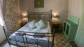 Un dormitorio con estructura de cama metálica, dos lámparas de noche, un armario verde y suelo estampado.