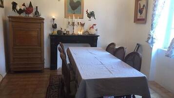 A dining room with a long table, chairs, a wooden cabinet, and wall-mounted decorations including roosters.