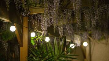 Een houten constructie met paarse bloemen en groene bladeren, verlicht door ronde lampen.