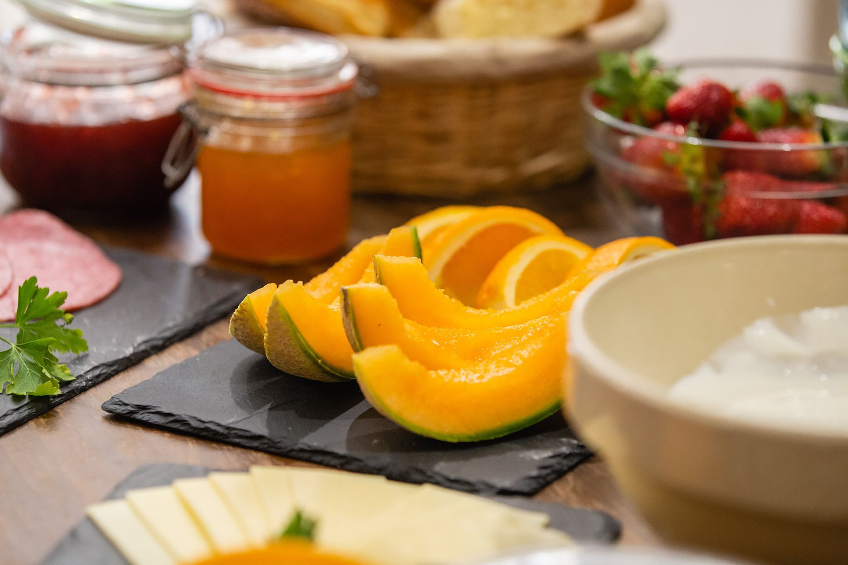 A table with sliced cantaloupe, honey jars, strawberries, and cheese.