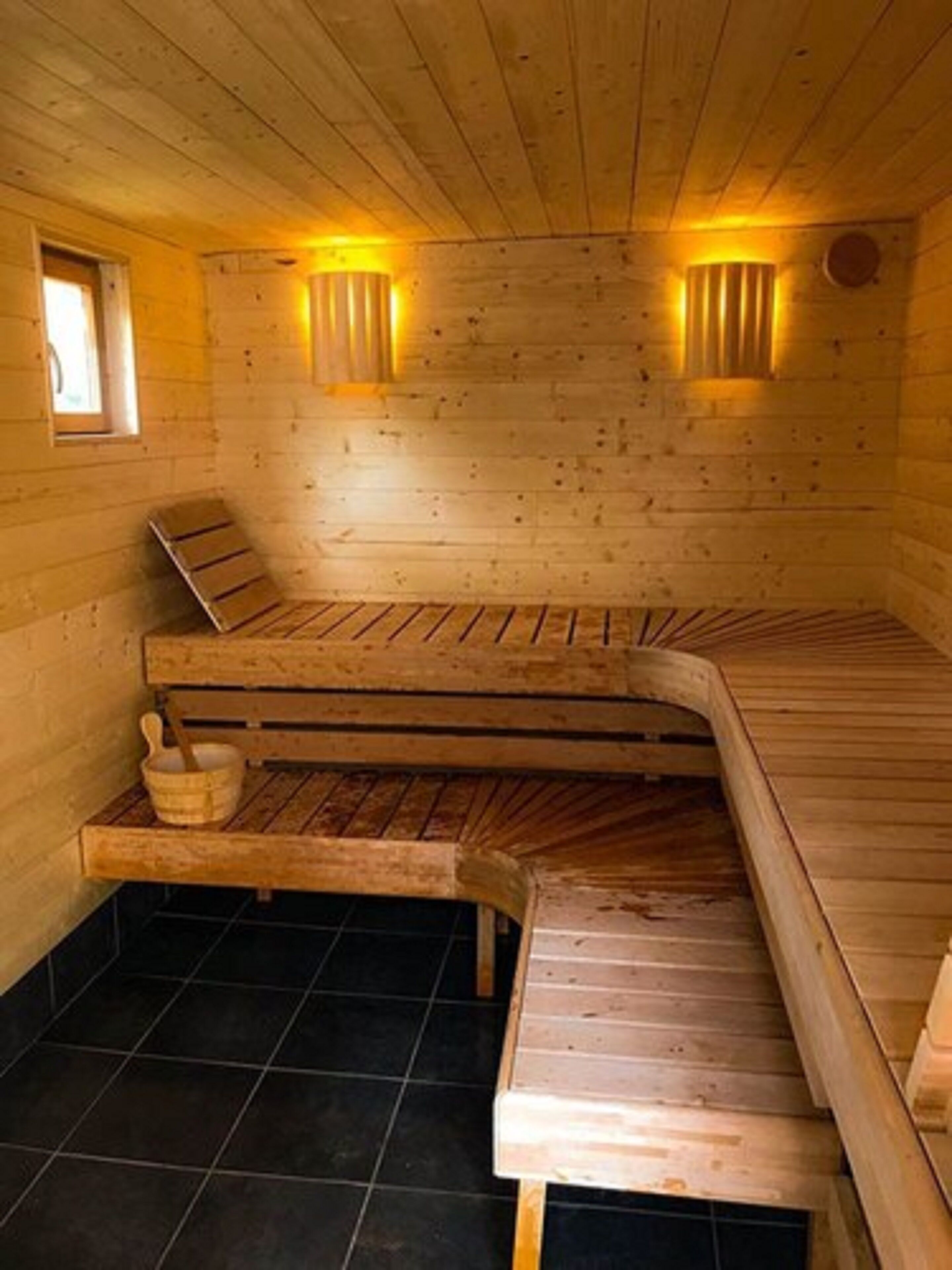 Una sauna de madera con bancos, una ventana pequeña e iluminación en la pared.