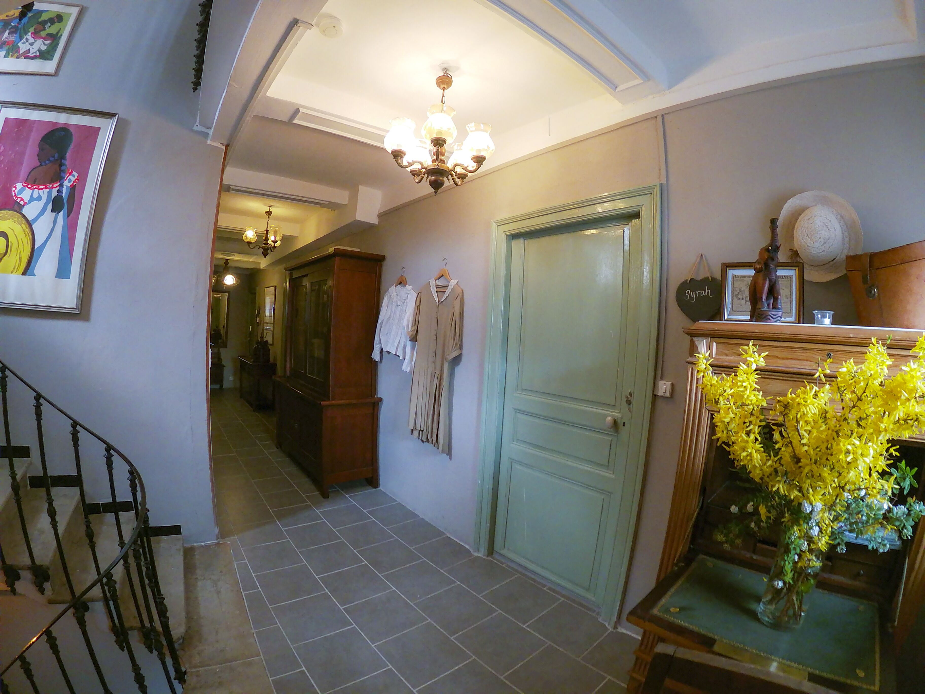 A hallway with a staircase, a green door, and a vase of yellow flowers on a table.