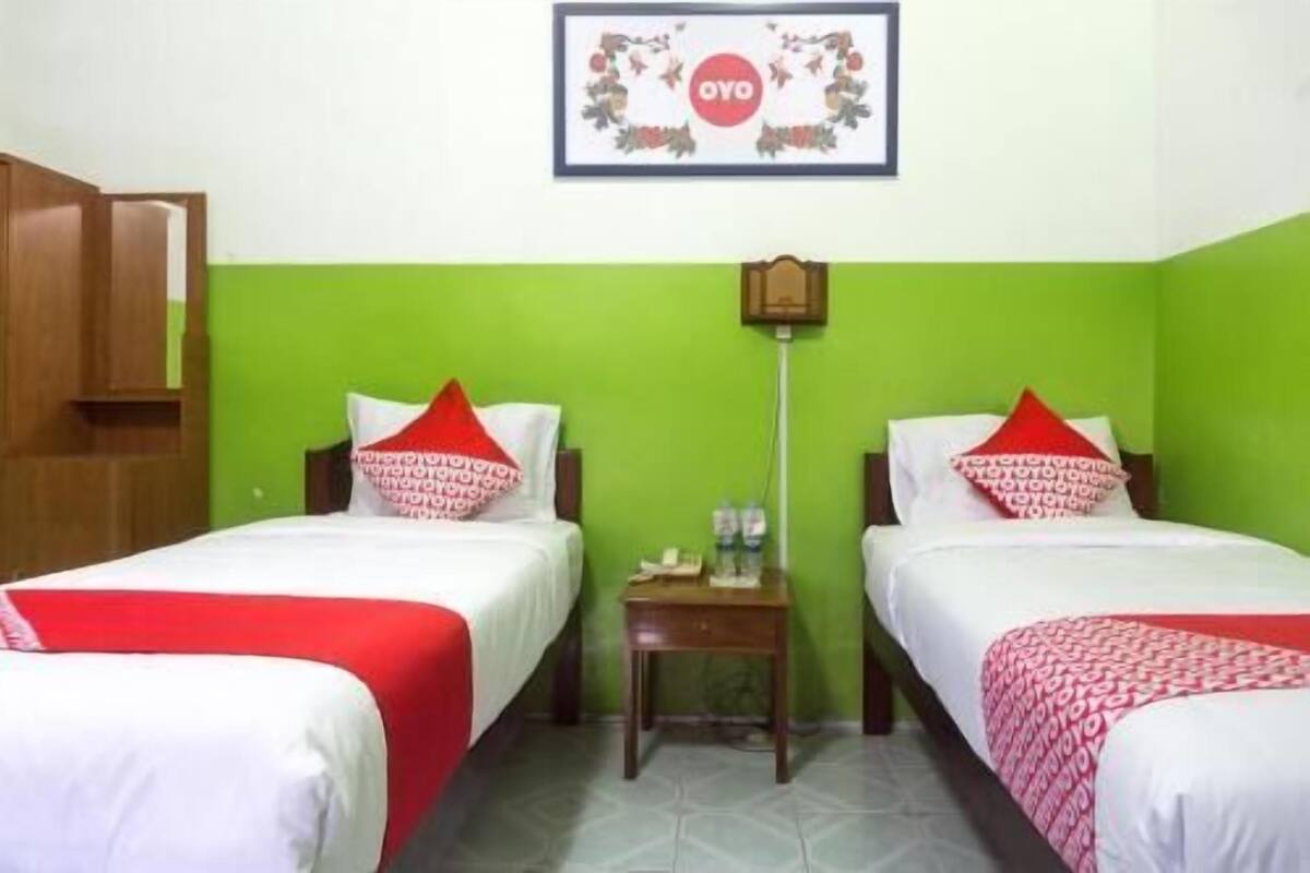 A hotel room with two beds, each with a red and white bedspread, a wooden nightstand between them, and a framed sign above the beds.
