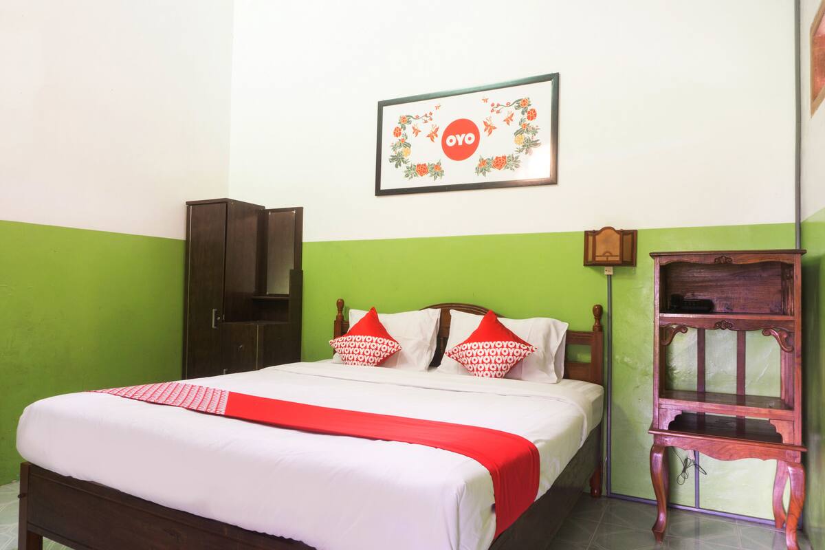 A neatly made bed with a red and white bedspread, a wooden headboard, and two decorative pillows.