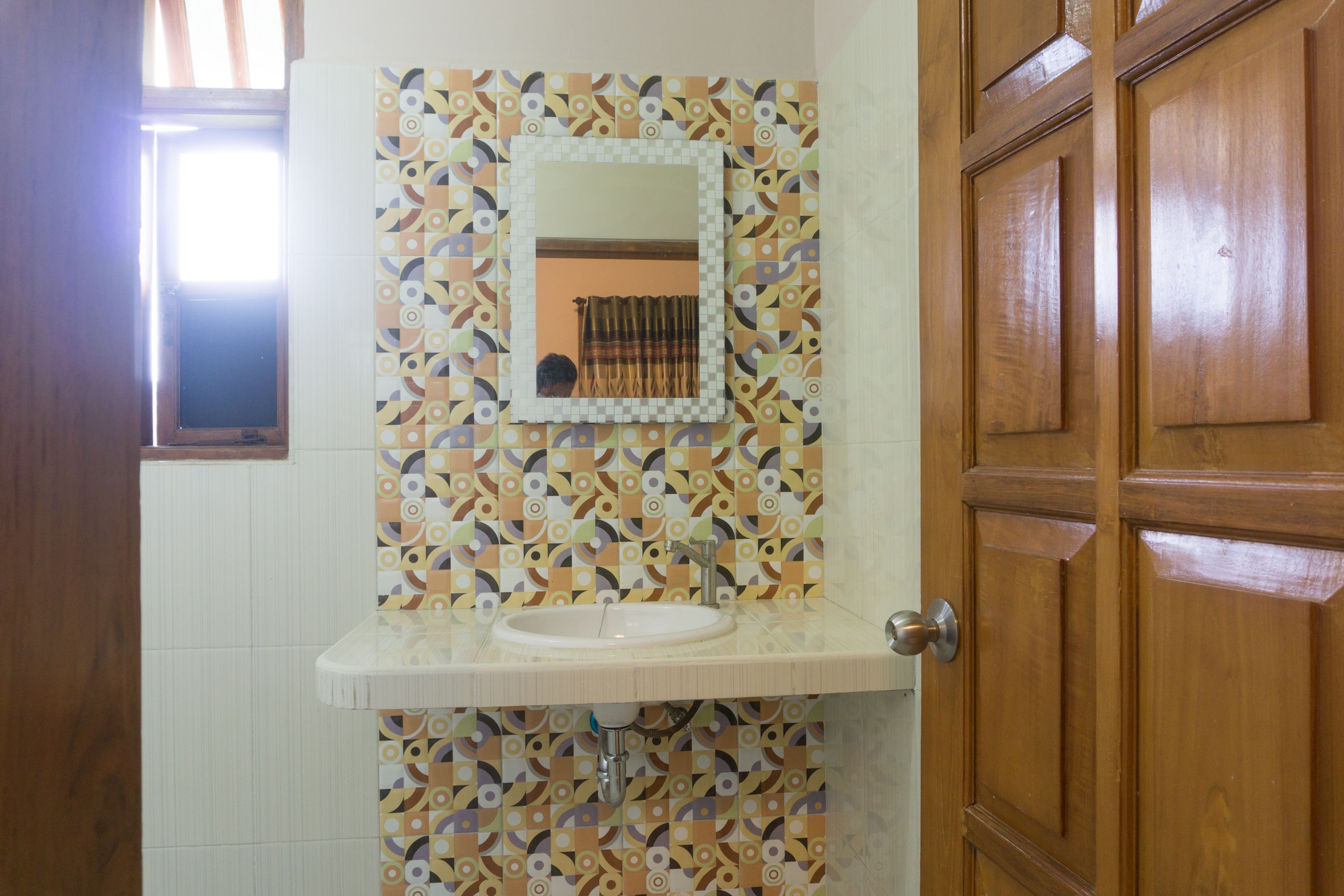 A bathroom with a patterned tile backsplash, a white sink, and a wooden door.
