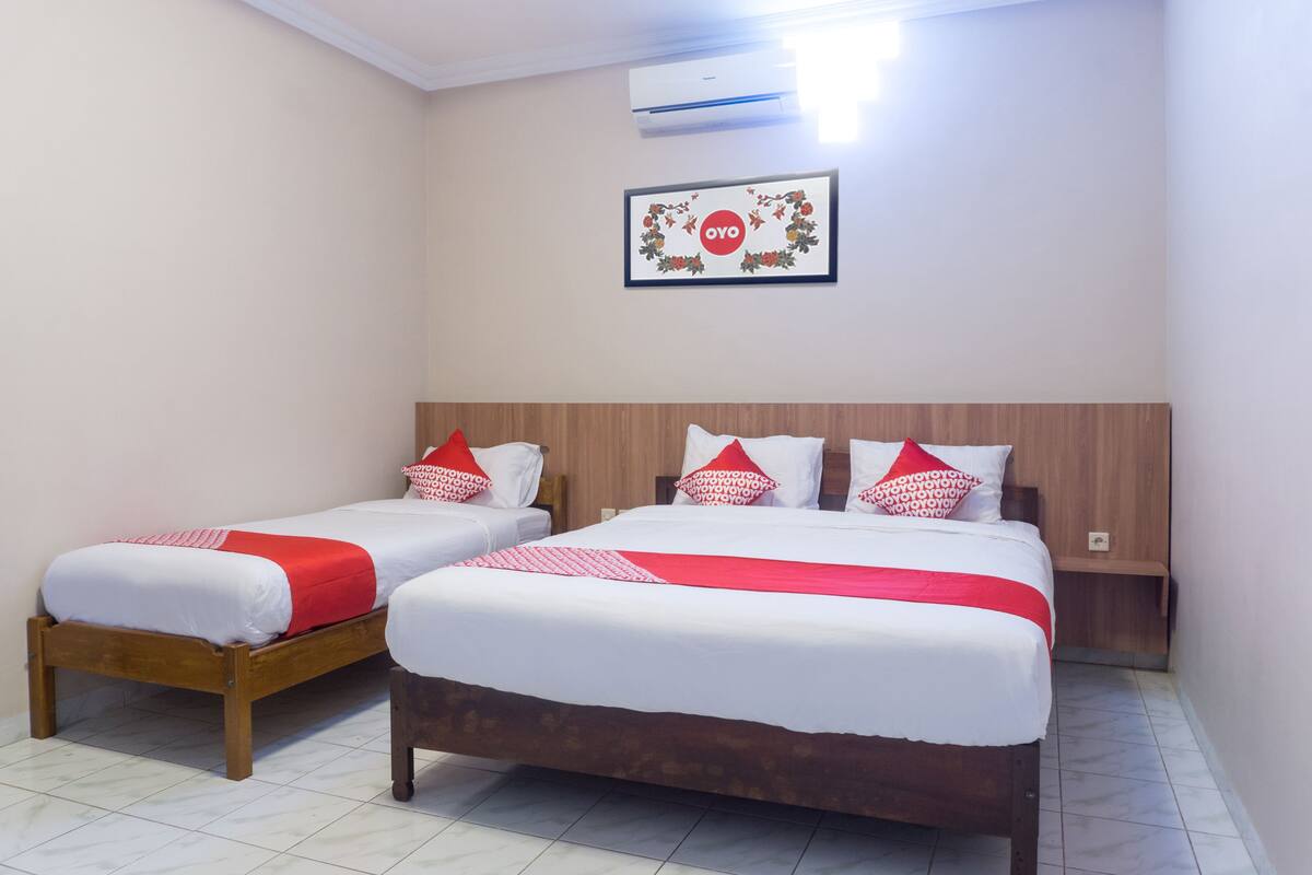 Two single beds with wooden frames and white bedding, a wooden headboard, a framed picture on the wall, and an air conditioning unit.
