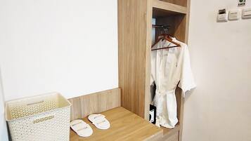 Een houten bank met een witte mand en slippers, een houten garderobe met kledingrek, en een witte muur met een thermostaat.