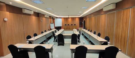 A conference room with long tables, black chairs, a whiteboard, and a projector screen.