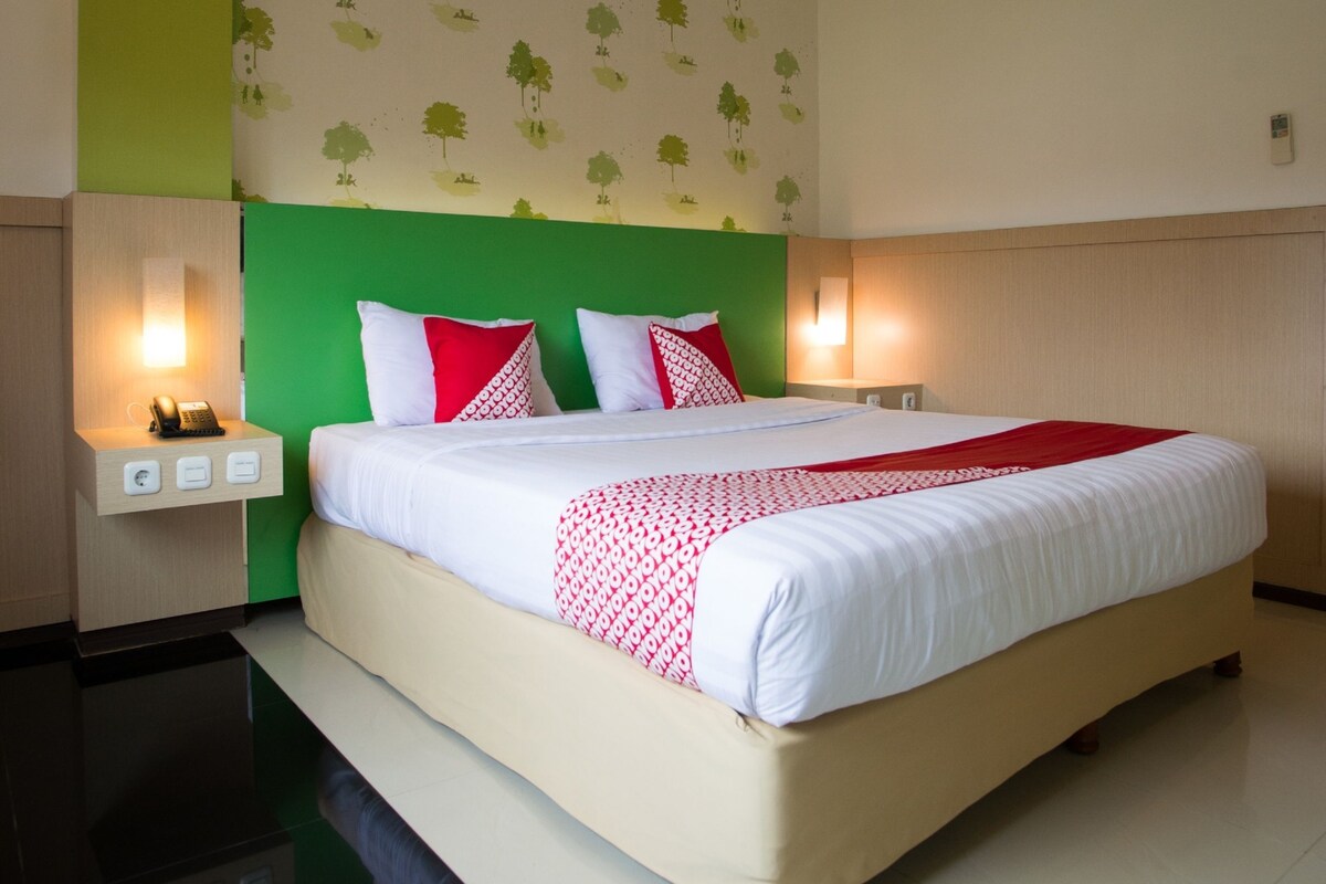 Een hotelkamer met een groot bed, een groen hoofdeinde, witte beddengoed en een muur met boommotieven.