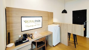 A hotel room with a wooden desk, a white refrigerator, a coffee maker, and a sign that reads "ROYAL PARK HOTEL Hospitality with Heart". - Royal Park Hotel (Samarinda)