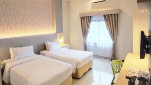 A hotel room with two beds, a desk, a chair, an air conditioning unit, and a window with curtains. - Royal Park Hotel (Samarinda)