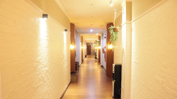 A hallway with wooden flooring and white brick walls, featuring wall-mounted lights and a hanging plant. - Royal Park Hotel (Samarinda)
