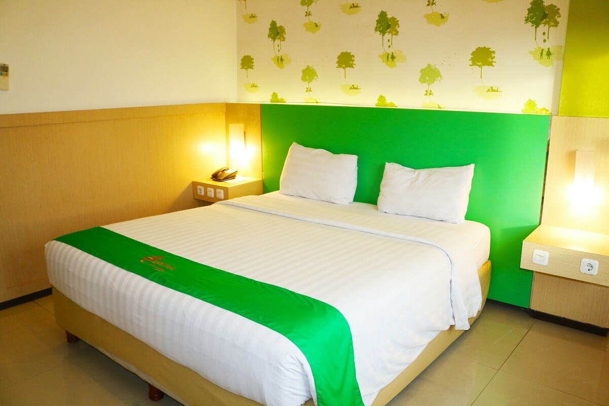 Een hotelkamer met een bed, een groen hoofdeinde, witte beddengoed en een muur met boomstickers.