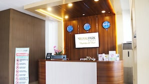 A reception desk at the Royal Park Hotel with a wooden finish, three clocks, and a signboard with hotel information. - Royal Park Hotel (Samarinda)