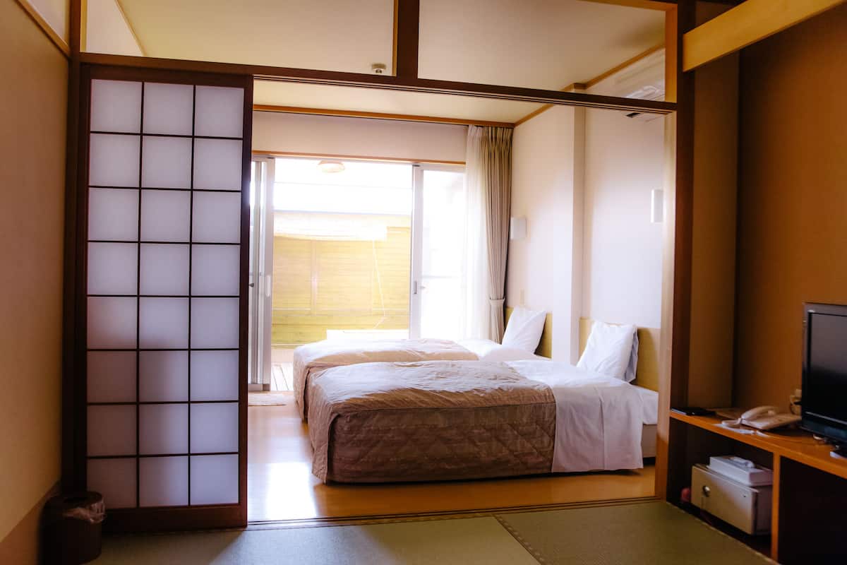A hotel room with two beds, a television, and a sliding door leading to a balcony.