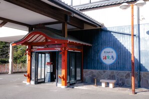 A traditional Japanese building with a red and white entrance, a stone wall, and a stone bench outside. - Hotel Tenzankaku Yurakuan (Shirahama)