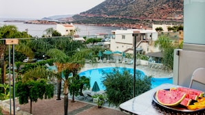 Uma área de piscina com espreguiçadeiras, uma mesa com frutas e vista para o mar e montanhas.