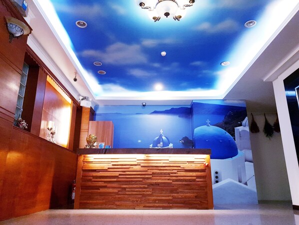 A reception area with a wooden reception desk, a ceiling mural depicting a night sky with clouds, and a cross on a dome structure.