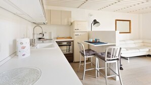 A compact kitchen with a sink, stove, and refrigerator, a dining area with a table and chairs, and a white sofa. - GuestHost - NEW! Exclusive Loft with balcony & garden! (Milano)