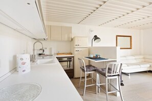 A compact kitchen with a sink, stove, and refrigerator, a dining area with a table and chairs, and a white sofa. - GuestHost - NEW! Exclusive Loft with balcony & garden! (Milano)
