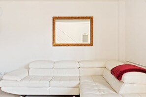 A white leather sofa with a red throw blanket, a gold-framed mirror on the wall, and a white wall. - GuestHost - NEW! Exclusive Loft with balcony & garden! (Milano)