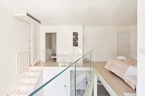 A modern hotel room with a glass railing, a bed with a patterned bedspread, and a view of the hallway. - GuestHost - NEW! Exclusive Loft with balcony & garden! (Milano)
