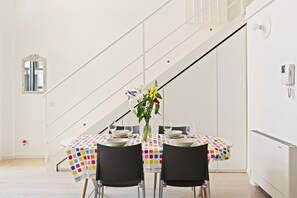 A dining area with a table set for two, a vase with flowers, and a staircase in the background. - GuestHost - NEW! Exclusive Loft with balcony & garden! (Milano)