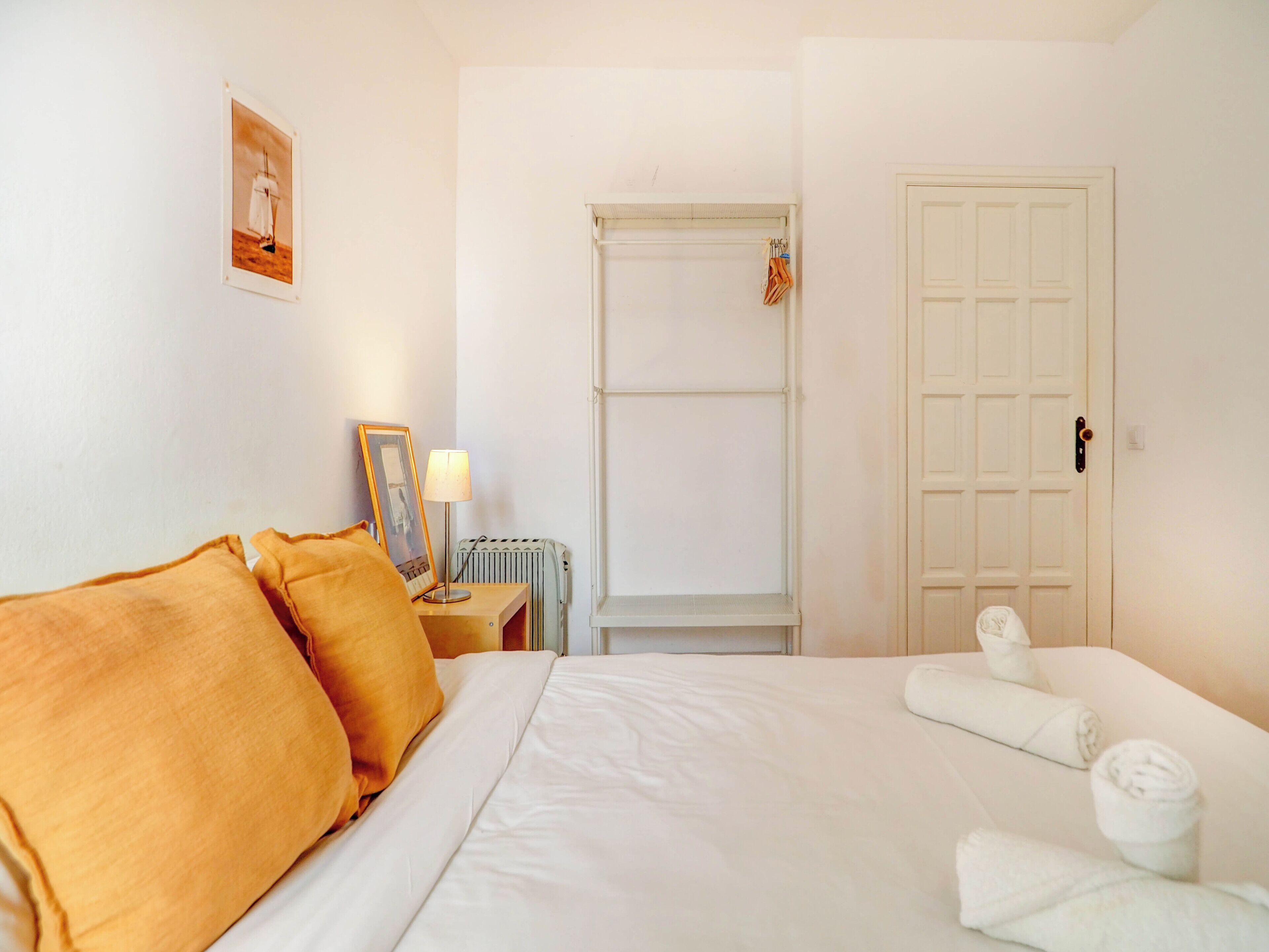 Une chambre d’hôtel avec un lit, une table de chevet, un tableau encadré, un radiateur et une porte.