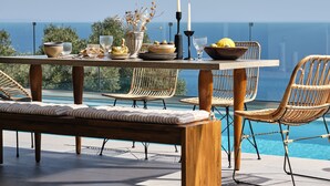 Una mesa de comedor con sillas y un banco, frente a una vista del mar.