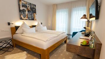A modern hotel room with a large bed, bedside table, and a desk with a lamp.