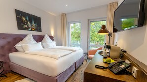 Habitación de hotel con cama, escritorio, teléfono, televisor y un cuadro de un paisaje urbano.