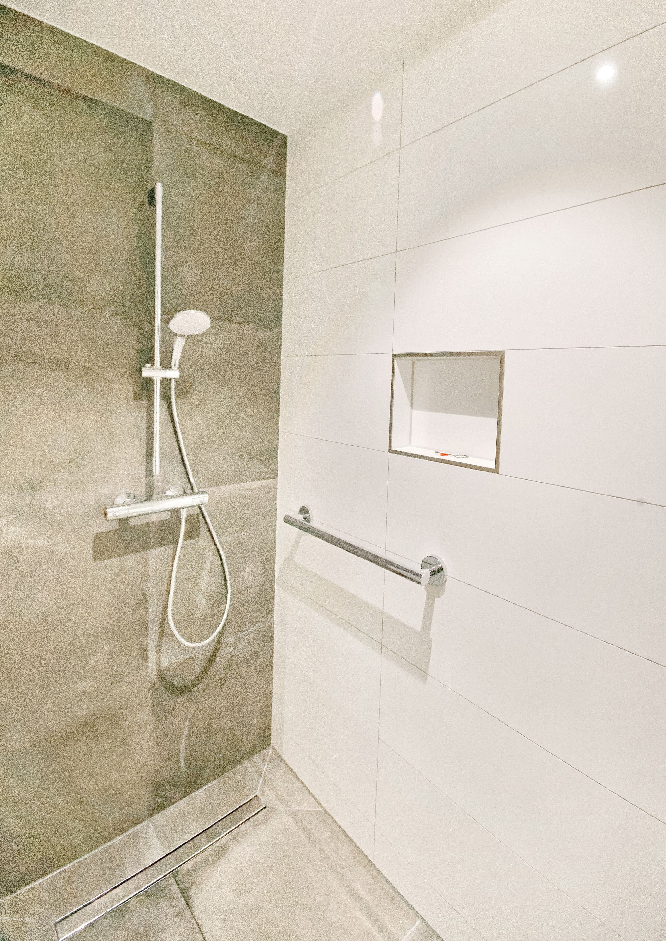 A bathroom with a shower, a handrail, and a small mirror on the wall.