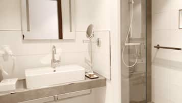 Un baño moderno con lavamanos blanco, espejo y ducha con cerramiento de vidrio.