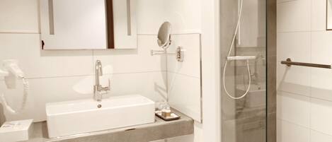 A modern bathroom with a white sink, mirror, and glass-enclosed shower.