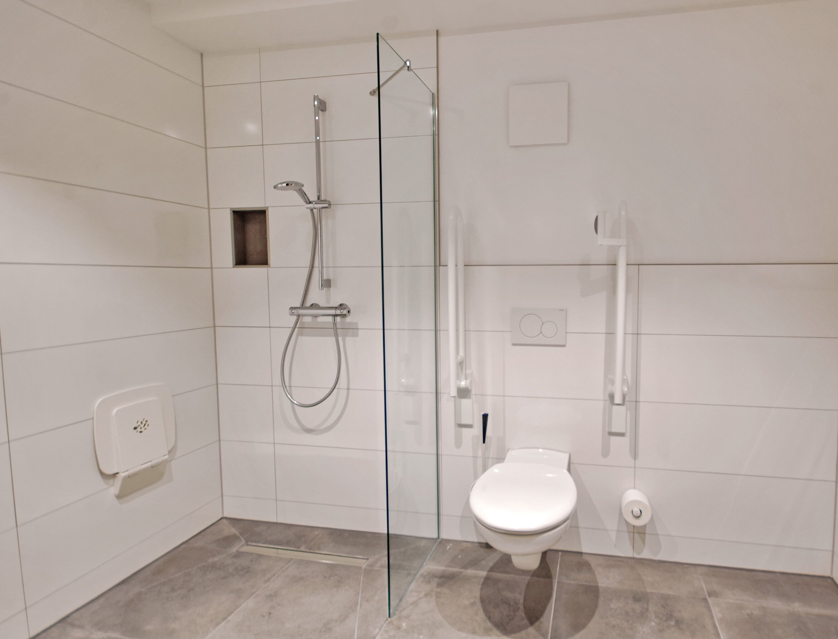 A modern bathroom with a glass-enclosed shower, a toilet, and a hand dryer.