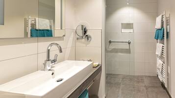 Un baño moderno con lavamanos, espejo y zona de ducha blancos.