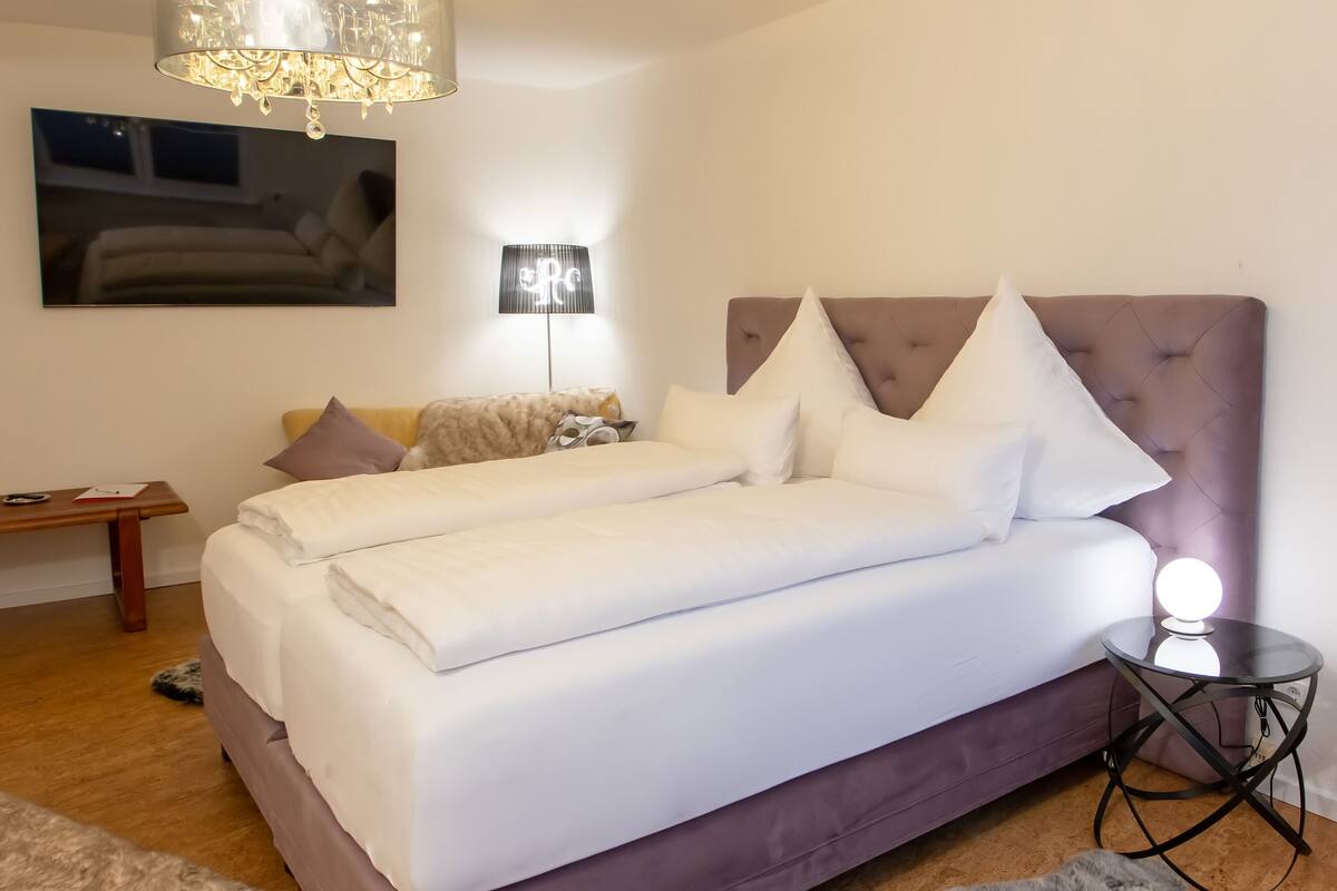 A modern bedroom with a large bed, a bedside lamp, and a chandelier.