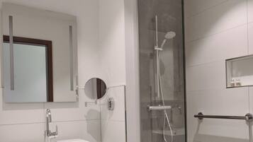 Un baño moderno con ducha de vidrio, lavamanos con espejo y un cubo de basura.