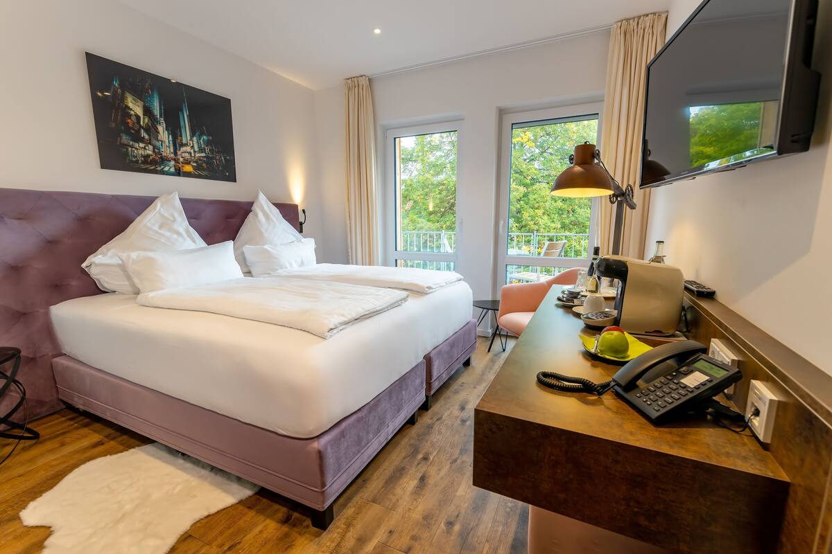 A hotel room with a bed, desk, telephone, and a large window with a view.