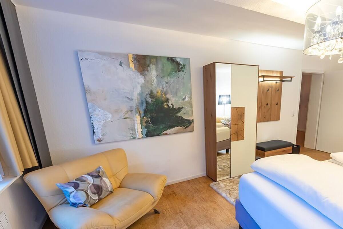 A hotel room with a bed, a sofa, a large abstract painting, a mirror, and a chandelier.